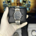 Silver watch held by a gloved hand with a blurred background